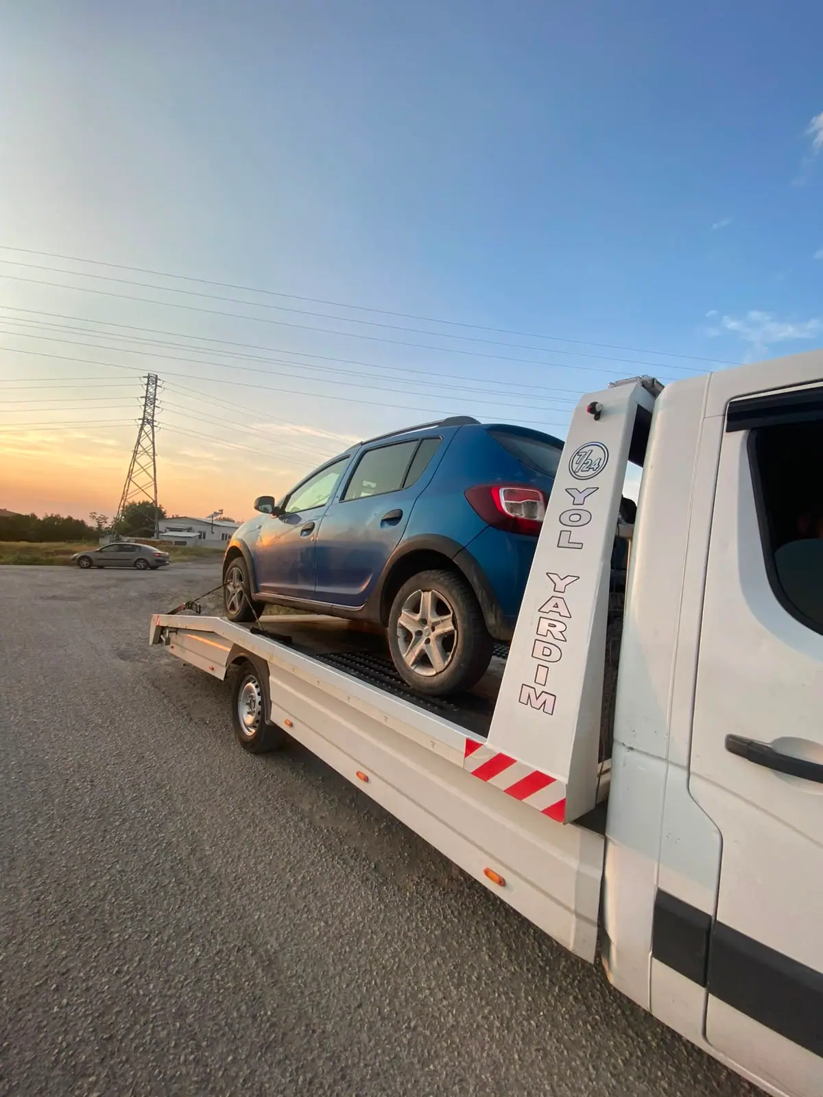 Gün batımında yol kenarında çekici platformunda taşınan mavi hatchback otomobil