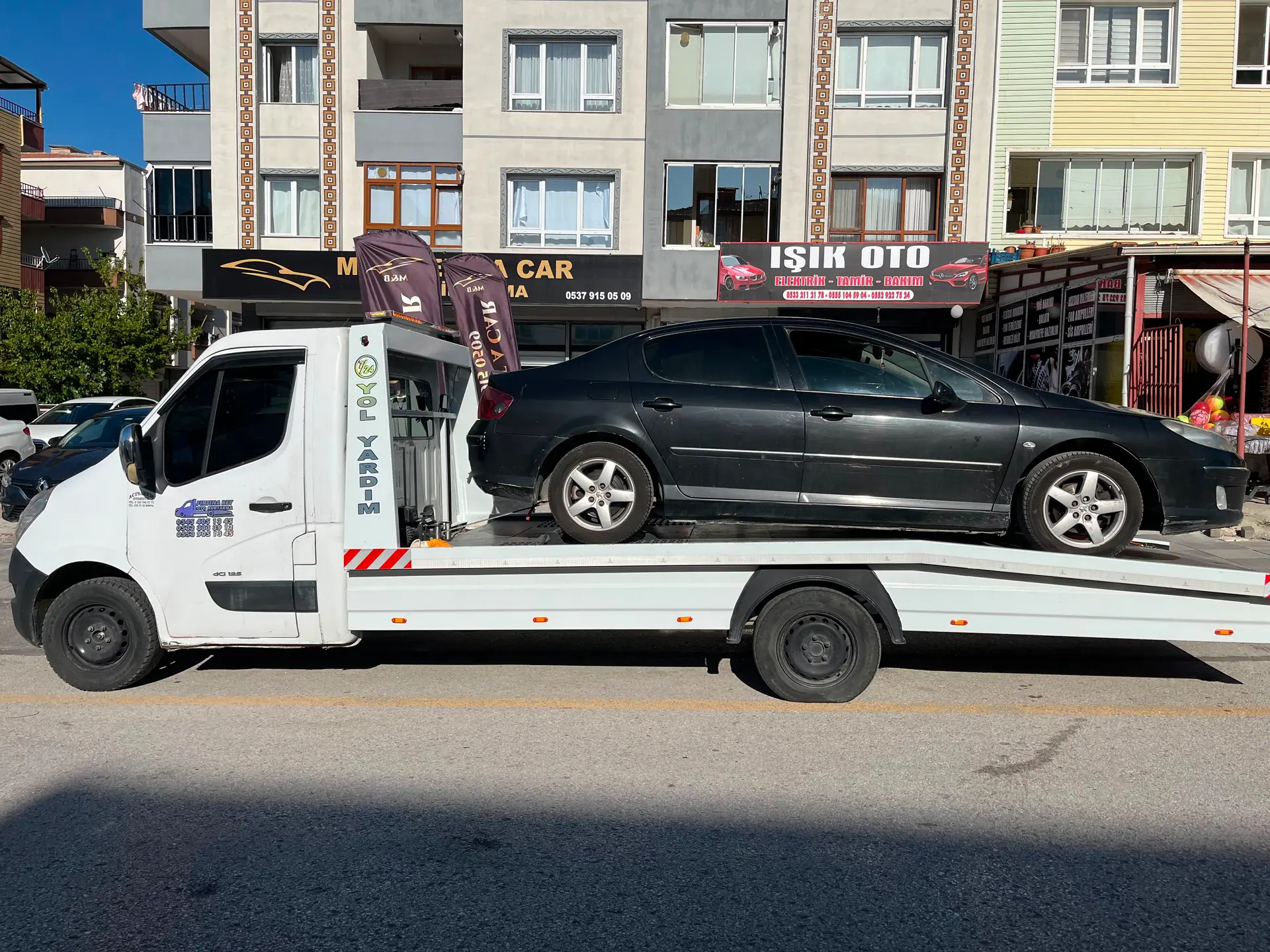 Çekici platformunda taşınan siyah sedan otomobil, cadde üzerinde yandan görünüm