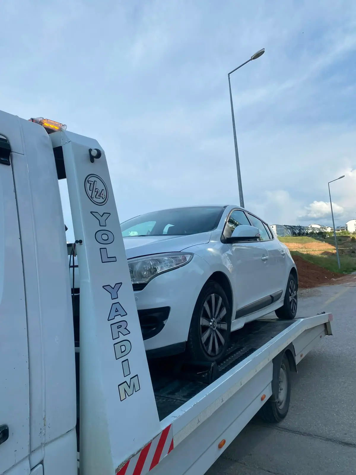 Yol kenarında çekici platformunda taşınan beyaz binek otomobil