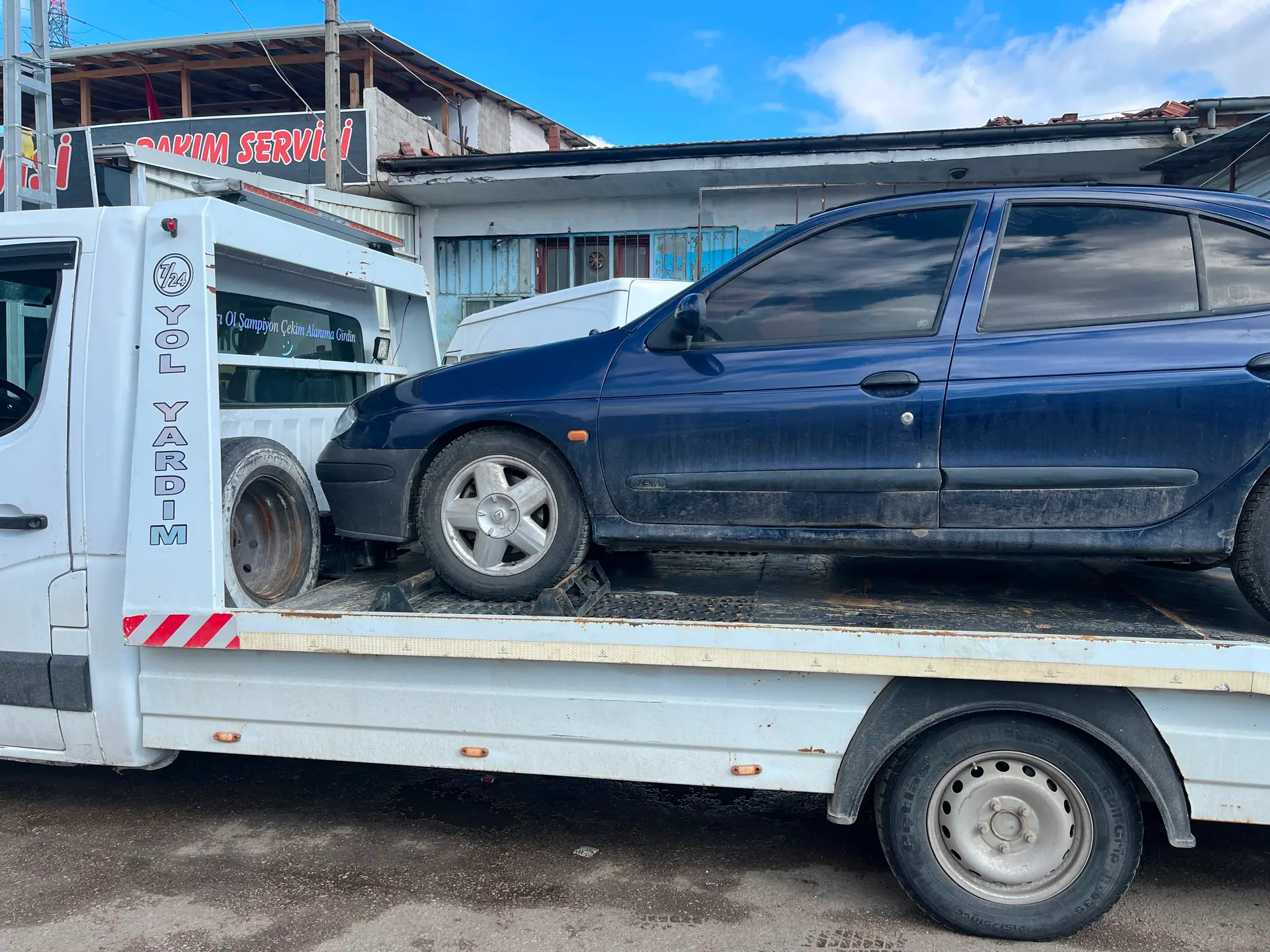 Oto bakım servisi önünde çekici platformunda taşınan lacivert sedan otomobil