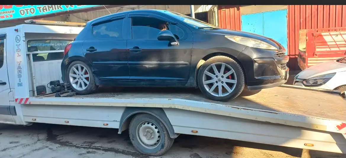 Oto tamir servisi önünde çekici platformunda duran siyah hatchback otomobil